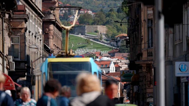 Sarajevska ulica s tramvajem, prolaznicima i brdima u pozadini.